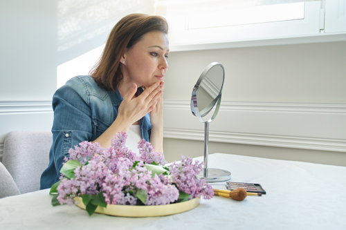 mature woman with make-up mirror massaging her face and neck mature woman with make-up mirror massaging her face and neck